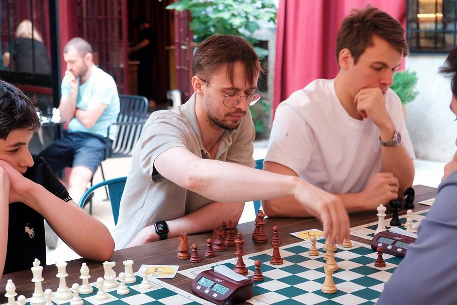 Igor Shatsev reaching across a tournament board to make a move, other players watching.